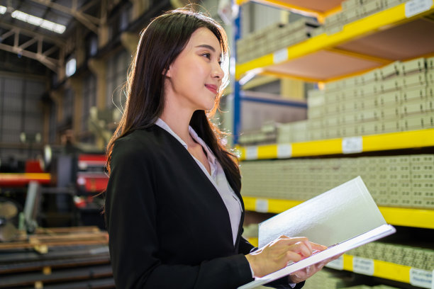 亚洲美丽的商业女性在工业制造工厂工作。迷人的女工业工厂工程师穿着正装，快乐地在工厂仓库处理订单和产品。图片下载