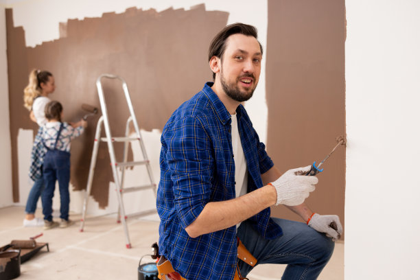 一名身穿格子衬衫、白t恤和牛仔裤的中年男子，右手拿着一个小油漆滚筒。他坐在他的腿上微笑着图片下载