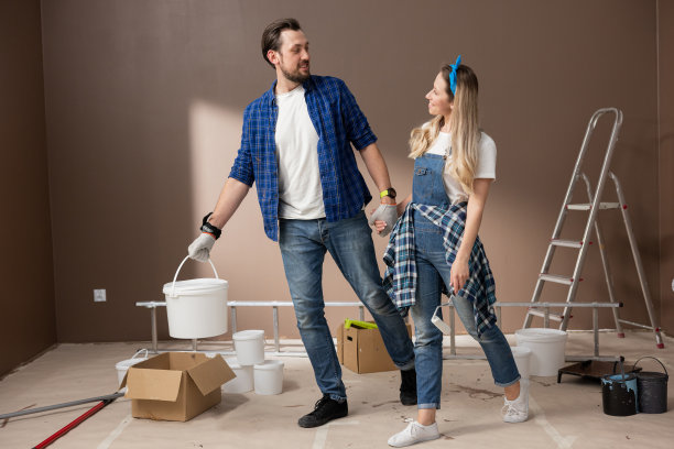 帅哥拥抱微笑着的美女，他们手里拿着墙漆辊罐，夫妻俩手牵着手，一起装修新公寓，刷新墙壁颜色图片下载