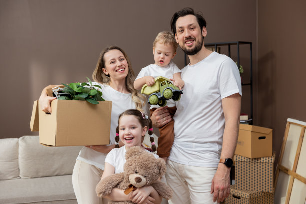 在搬家的日子里，充满爱的一家人带着箱子搬进新家，年轻父母和年幼的孩子相爱的画像图片下载