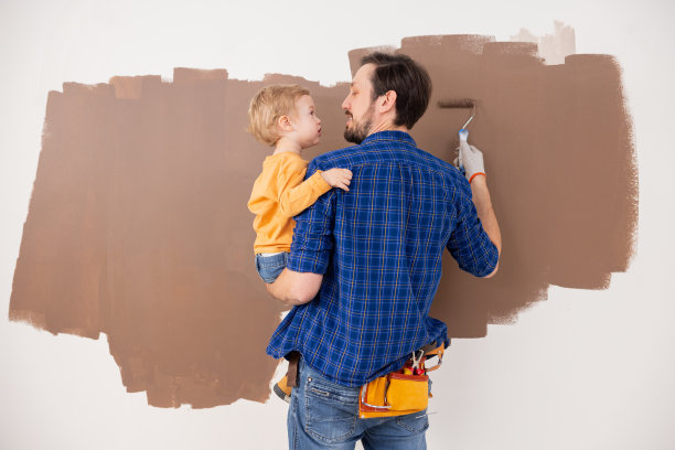 一位父亲抱着他的小儿子，他们一起画出了棕色的云朵。那个小孩穿着一件橙色的衬衫，那个男人穿着一件蓝色的格子衬衫。这张照片是从背面拍的图片下载