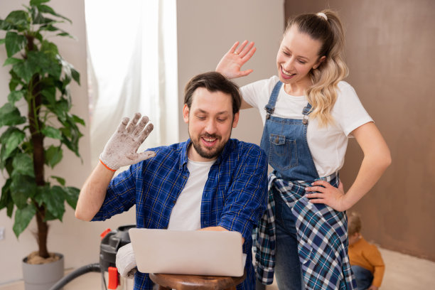 身穿牛仔布和格子衬衫的两名英俊的年轻人正在和朋友们视频聊天，向他们展示装修后的房子。图片下载