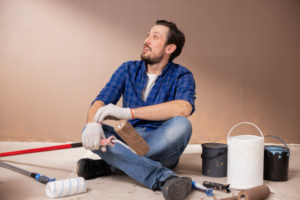 一名留着大胡子的37岁男子惊讶地望向右边。他手里拿着一个油漆滚筒，他的公寓已经开始装修图片下载