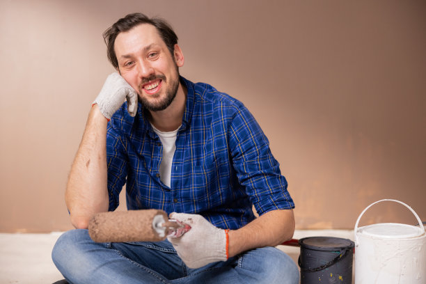 一个留着胡子的男人微笑着用右手托着脸。他左手拿着一个油漆滚筒，开始装修他的新房子，这是他贷款买的图片下载