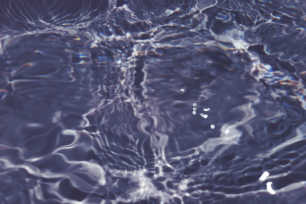 离焦模糊透明蓝色清澈平静的水面纹理与飞溅和气泡。新潮抽象的自然背景。阳光下的水波与复制空间。蓝色水彩闪亮的图片下载