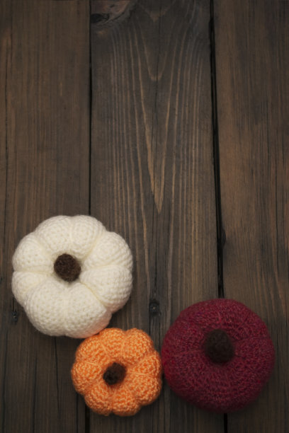 三个用钩针编织的南瓜放在木桌上。在一张木桌上，编织的南瓜排成一排。橙色。白纱红纱，用自己的双手。万圣节的秋季装饰。图片下载