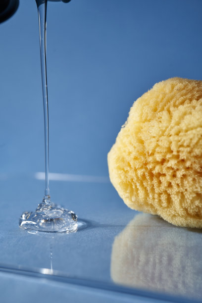 一块天然海绵和一滴蓝色背景的啫喱或洗发水。图片下载