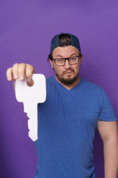 英俊的年轻人房地产经纪人手持巨大的钥匙为新地主穿着随意孤立紫色背景。大个子拿着大钥匙。房地产的概念。年轻的房地产老板。图片下载