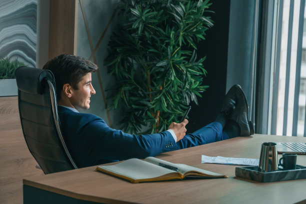 西装革履的商人手里拿着手机。男人打字留言，使用社交网络。检查消息。商务会议。现代办公室。总经理、首席执行官。打电话来的合作伙伴。计划工作时间图片下载