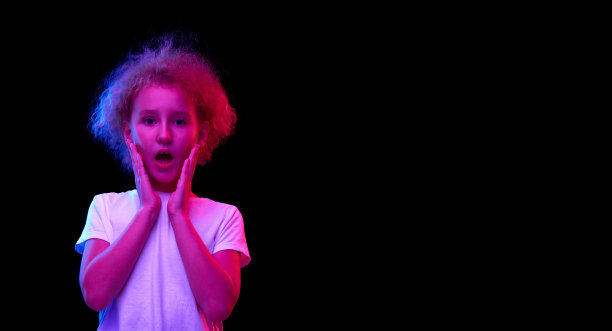 震惊的小女孩，在白色t恤的孩子看着相机惊讶地孤立在粉红色霓虹灯的黑暗背景。图片下载