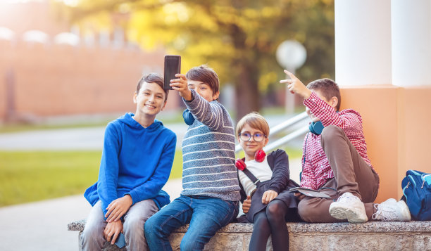 孩子们背着背包，戴着耳机坐在学校附近公园的长凳上图片下载