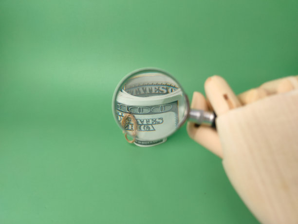 木制的手拿着放大镜，在绿色的背景上放大钞票。图片下载