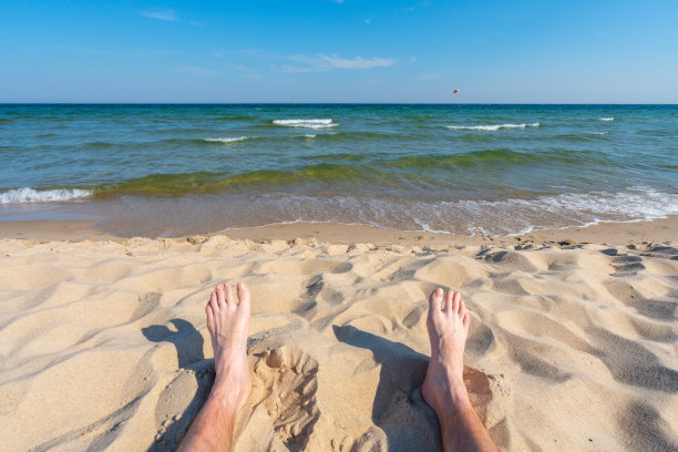 男性的脚在沙滩上与水颜色的海为背景。概念为休闲、娱乐、暑假、海滩度假。图片下载