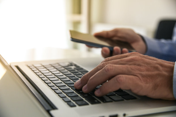 特写男子的手使用智能手机和笔记本电脑。商人用电脑和手机工作图片下载