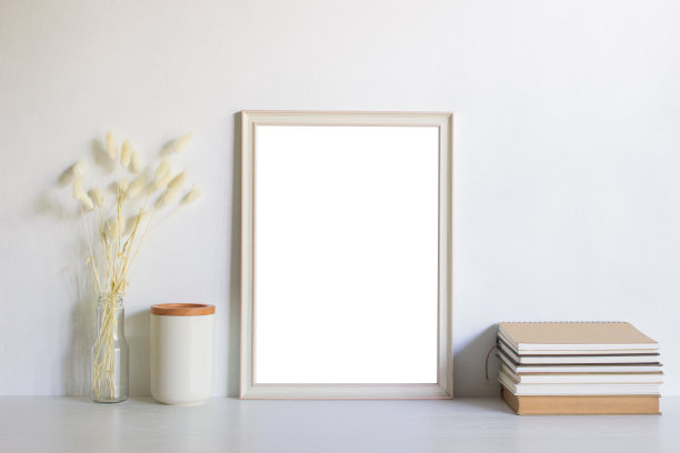 白色的木制相框和白色的花，书和杯子在白色的墙壁上，自然光线。图片下载