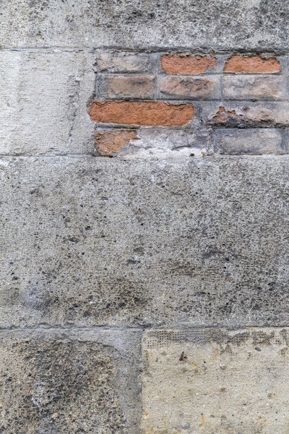 近距离纹理的风化，肮脏，石头砖墙。一个街区露出了红砖，旁边是一些混凝土修补。图片下载