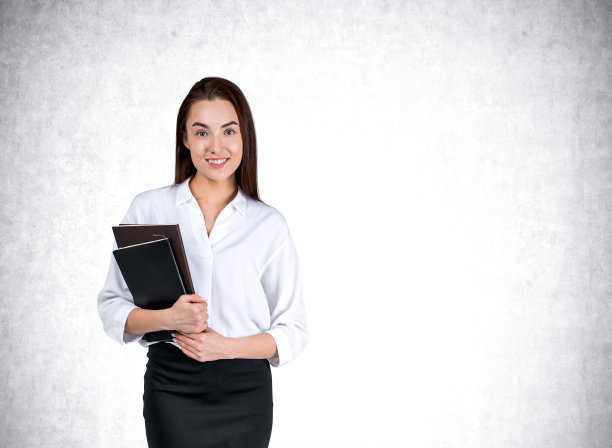 年轻的女商人与笔记本，微笑在灰色的墙背景图片下载
