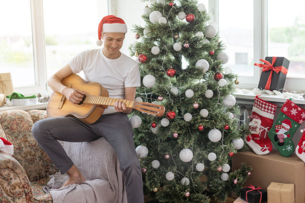 年轻英俊的男子坐在沙发上，他正弹着吉他，听着圣诞音乐，放松着概念图片下载