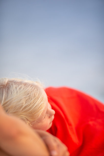 小女孩盖着红毯子躺在沙滩上休息图片下载