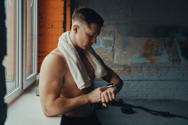 英俊的肌肉男站在健身房的窗户边看他的智能手表图片下载