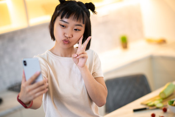 年轻女子在厨房用智能手机自拍图片下载
