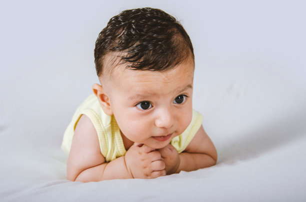 身穿黄色紧身衣的男婴趴在地上，头朝上，放在白色的摄影棚里图片下载