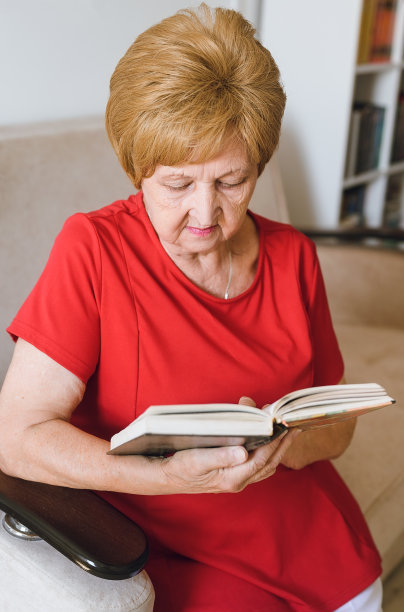 可爱的老妇人坐在家里的沙发上看书图片下载