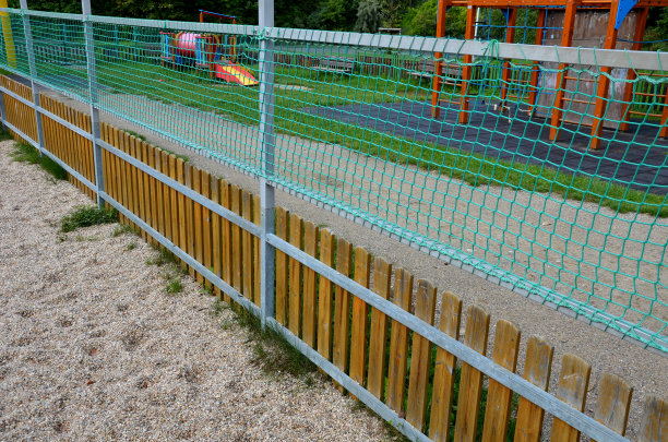 在儿童游乐场的木栅栏上方加装网。镀锌的金属框架用绿色的纺织网增加了栅栏的高度。沙盒图片下载