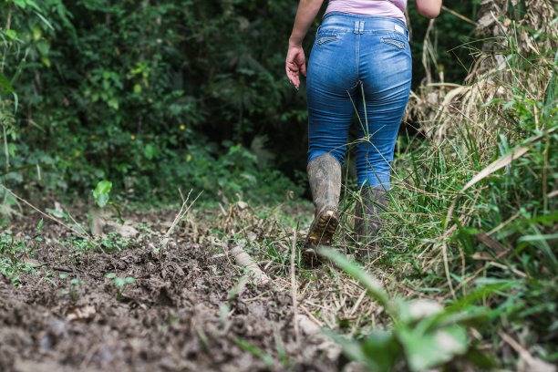 拉丁农妇，穿着黑靴子走在泥泞的路上。在哥伦比亚潮湿的丛林中，一个女孩穿过一条艰难的小路回家。一个女人独自在森林里迷路了。图片下载