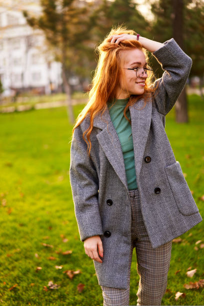 在阳光明媚的秋日里，红头发微笑着的漂亮女人走在公园里。优雅的女性姿势在时尚的真实的服装有有趣的笑绿色草坪与生动的树叶，树叶。女孩喜欢秋天。图片下载