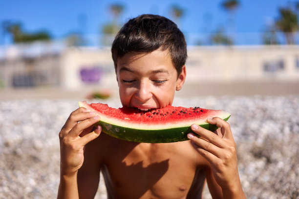 夏天，男孩在海滩上吃西瓜图片下载