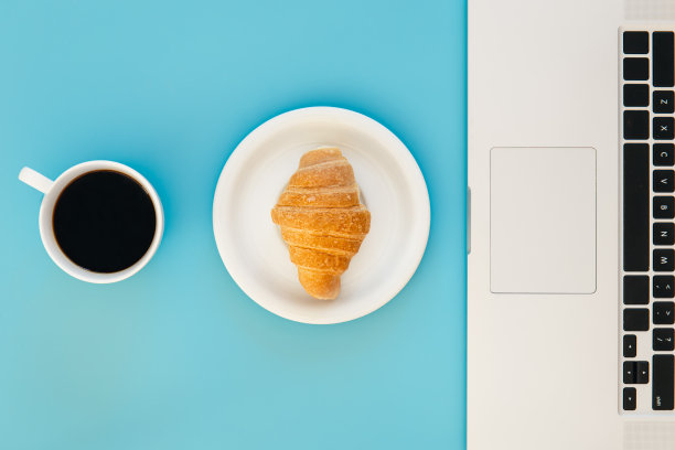 羊角面包，一杯咖啡，蓝色背景的笔记本电脑，平躺着。图片下载