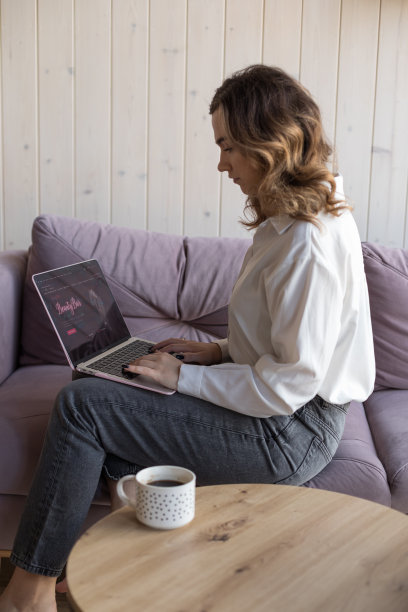 女人在现代笔记本电脑上工作的肖像坐在柔软的紫色沙发上，穿着休闲装，在桌子旁边的一杯咖啡。客厅设计高雅，装饰美观，自由复制空间图片下载