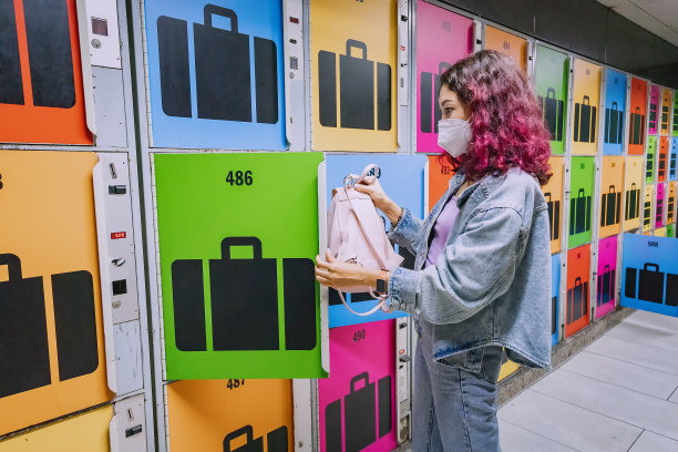 佩戴医用口罩的女性将行李放在火车站或机场的自动行李寄存处，以确保安全图片下载