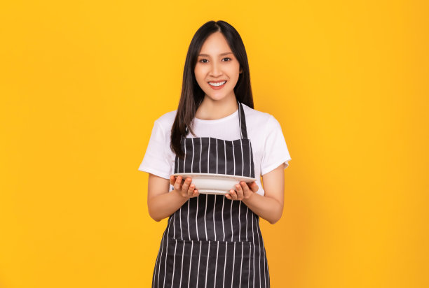 美丽的亚洲妇女穿着围裙，拿着黄底白盘。图片下载