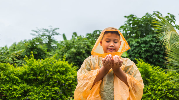 一个穿着橙色雨衣的亚洲男孩在雨天快乐地玩耍。图片下载
