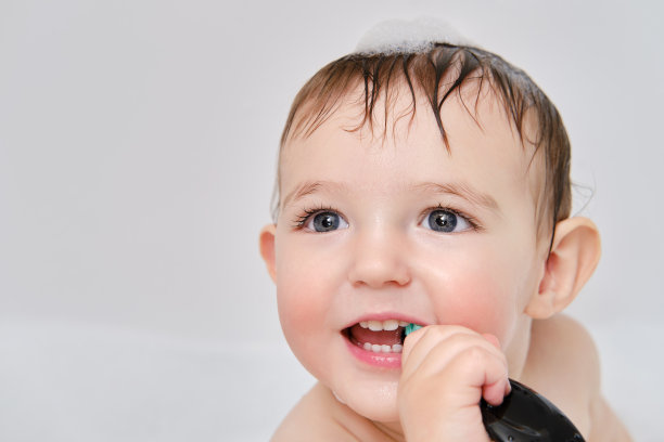 快乐的蹒跚学步的婴儿坐在泡泡浴里刷牙。这个孩子洗漱并学会用牙刷刷牙。一岁零三个月的孩子图片下载