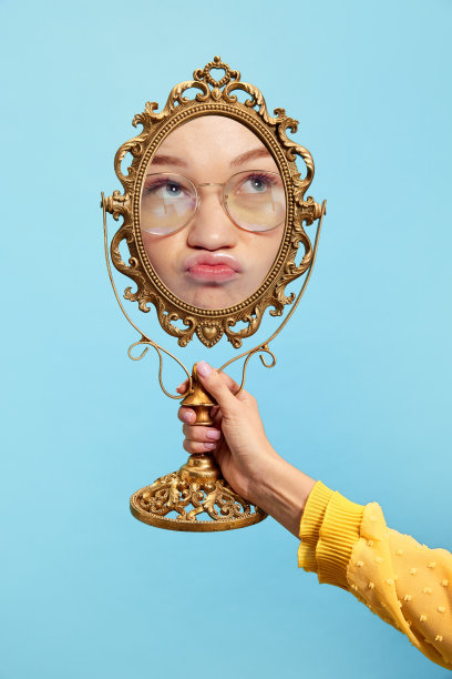 年轻的红发女孩手持复古风格的镜子，看着自己的倒影。美的概念，情感，艺术图片下载