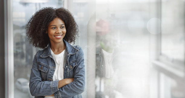 一个迷人的年轻非洲女商人在蓝色牛仔裤微笑着站在办公室的窗户图片下载