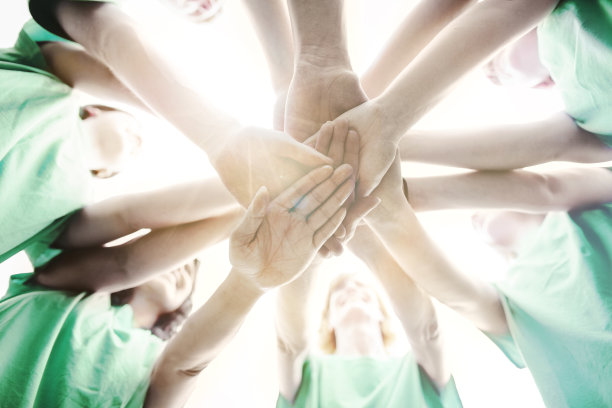 多种族群体的男性和女性在社区中堆叠双手，支持团队合作，成功，作为环境社会问题的志愿者与天空和阳光微笑图片下载