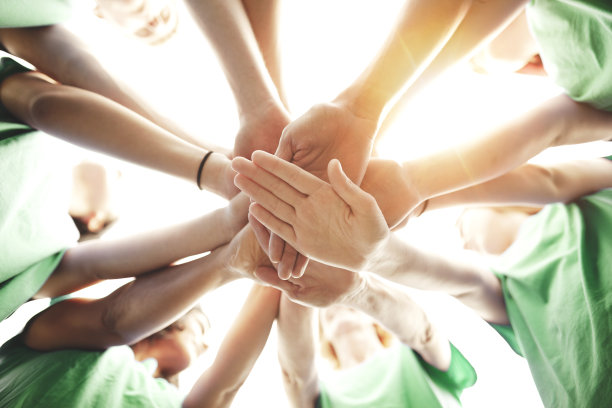 多种族群体的男性和女性在社区中堆叠双手，支持团队合作，成功，作为环境社会问题的志愿者与天空和阳光微笑图片下载