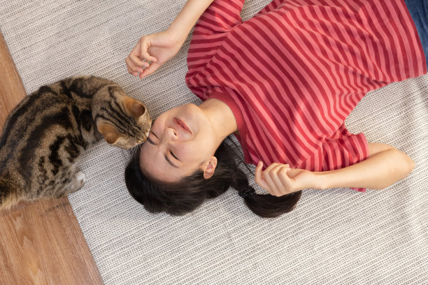亚洲妇女躺在地板上，一只猫亲吻她的脸颊图片下载