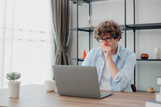 快乐的年轻白人男子戴着眼镜，微笑着在他的笔记本电脑上打字，在清晨用他的一杯咖啡完成他所有的业务。年轻白人在家在线学习。图片下载