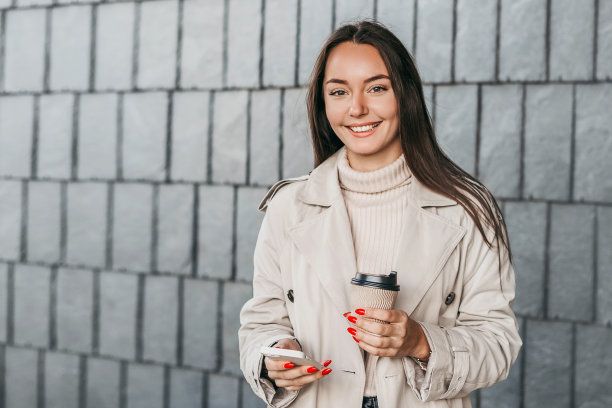 一个拿着智能手机的黑发女孩站在建筑正面的背景前微笑着。本空间图片下载