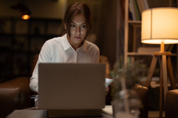 亚洲女性坐在办公桌前处理文书工作，在家里用电脑工作到深夜。图片下载