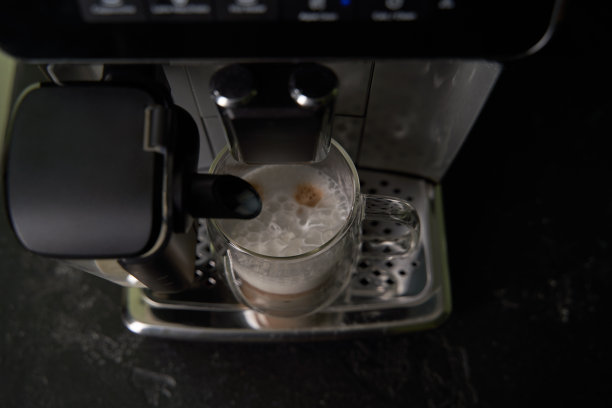 刚煮好的卡布奇诺从咖啡机里倒进玻璃杯里。图片下载