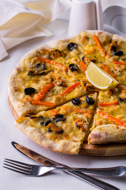 披萨配奶酪、贻贝、柠檬、番茄和胡椒，放在木板上，餐具放在白色的桌子上图片下载