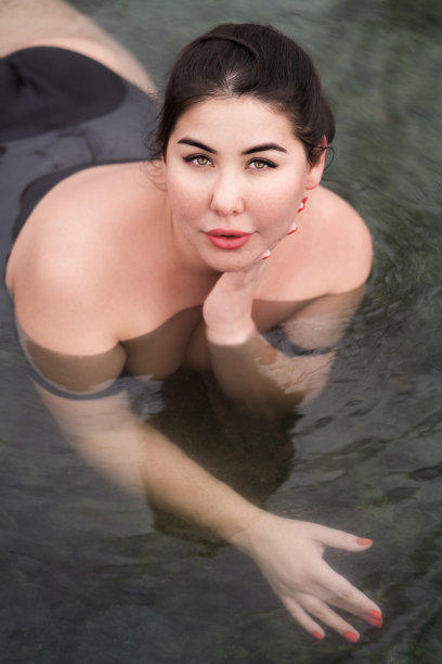 加码年轻女子与大胸部在黑色泳衣躺在户外游泳池在balnetherapy温泉图片下载