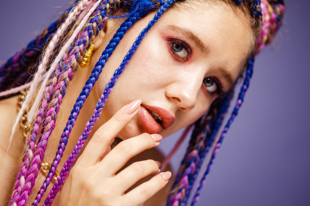 时尚的年轻女子，五颜六色的头发和非洲式的辫子，脏辫看着在镜头。图片下载