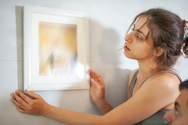 一对年轻夫妇把装框的照片挂在家里的墙上图片下载